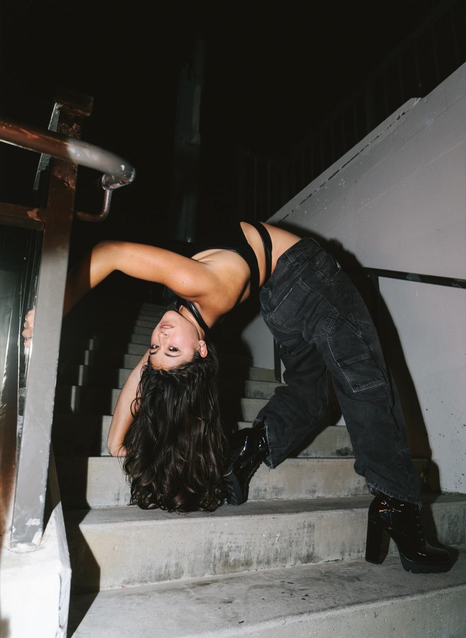 Anne Arellano in a handstand on a pedestal in white performance attire, one leg extended.