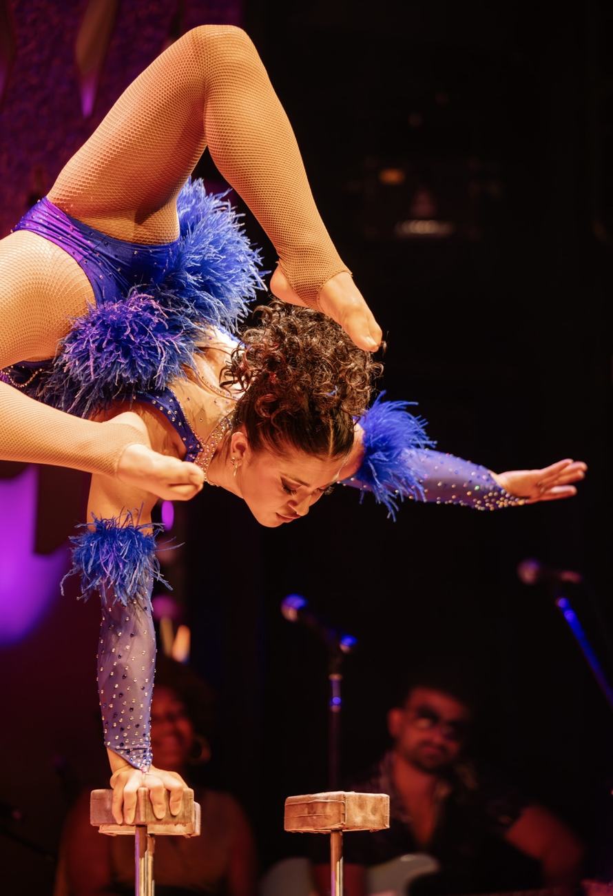 Anne Arellano in a feathered costume, deep backbend on two pedestals.